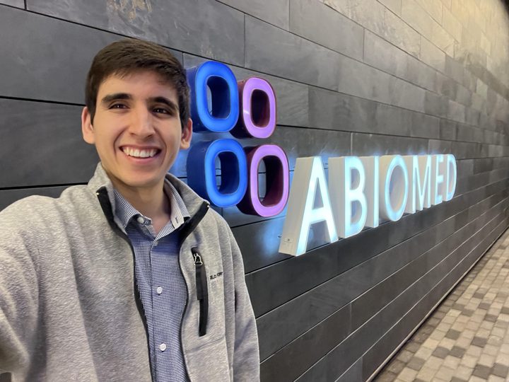 Jordon smiling beside the lit Abiomed sign in the company lobby