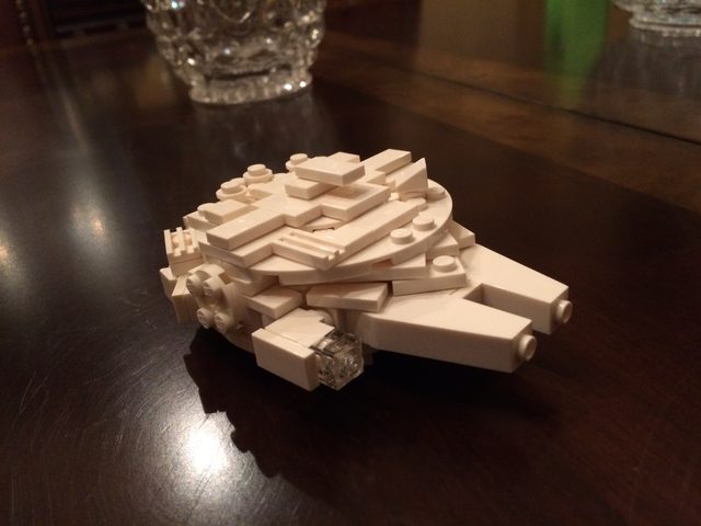 A small all-white LEGO model of the Millennium Falcon on a dark wood table