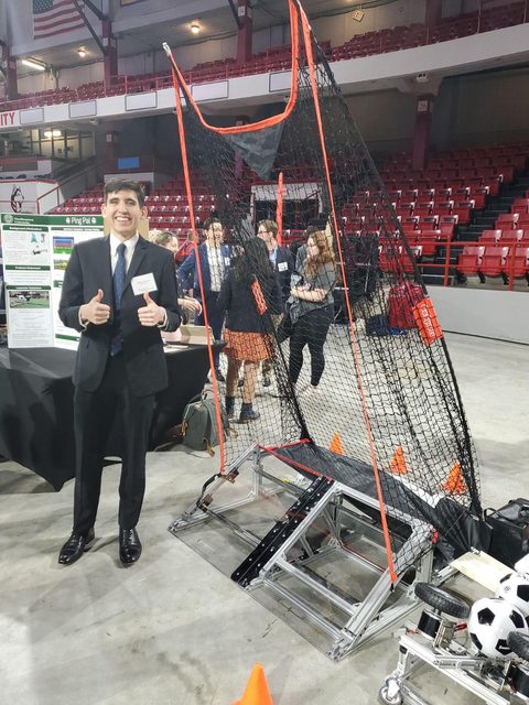 Jordon giving two thumbs up beside the Ping Pal goalie trainer at the capstone showcase