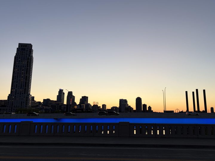 Minneapolis skyline at sunset from a bridge lit in blue